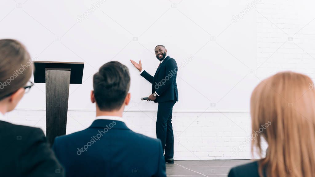 smiling handsome african american speaker talking during seminar in conference hall and pointing on screen