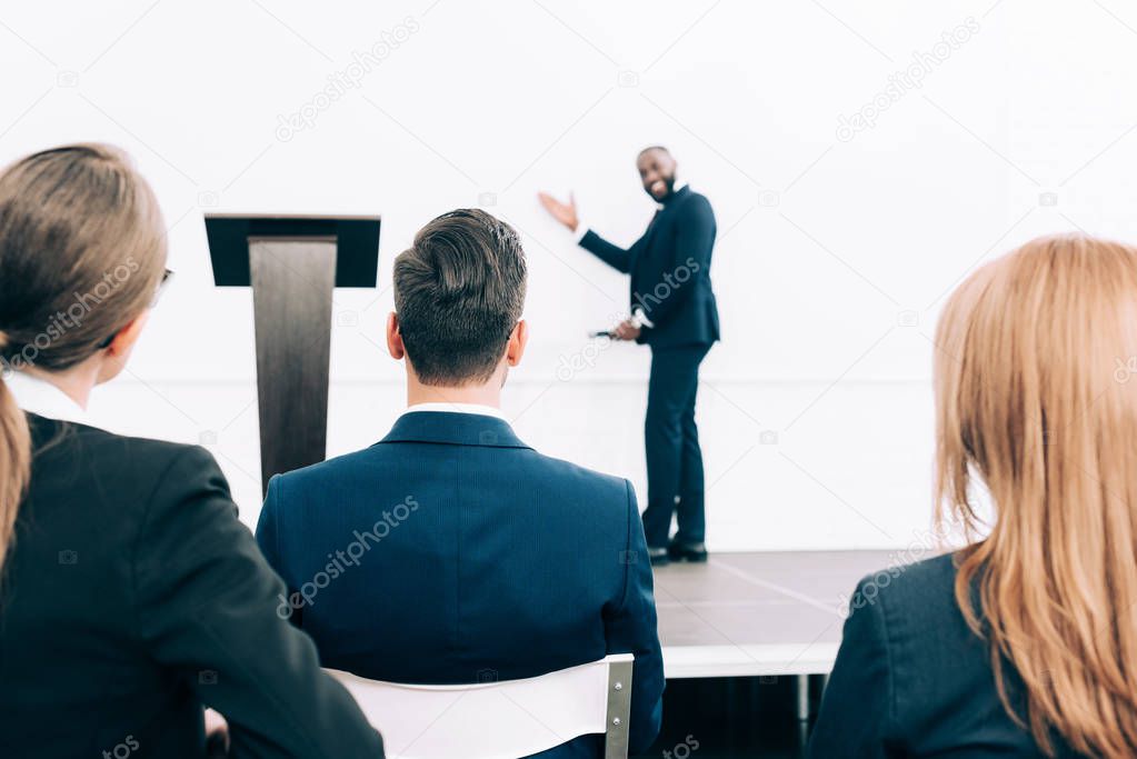 selective focus of smiling african american speaker pointing on screen in conference hall