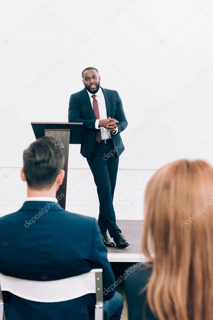 handsome african american speaker leaning on podium tribune during seminar in conference hall