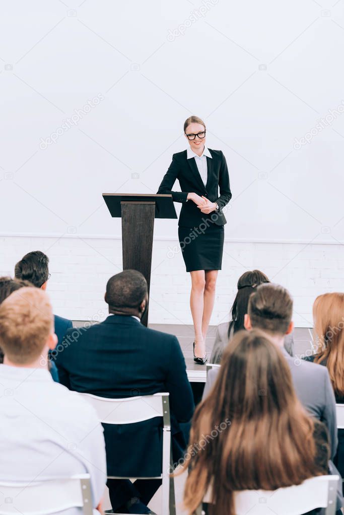 smiling attractive lecturer looking at multiethnic audience during seminar in conference hall