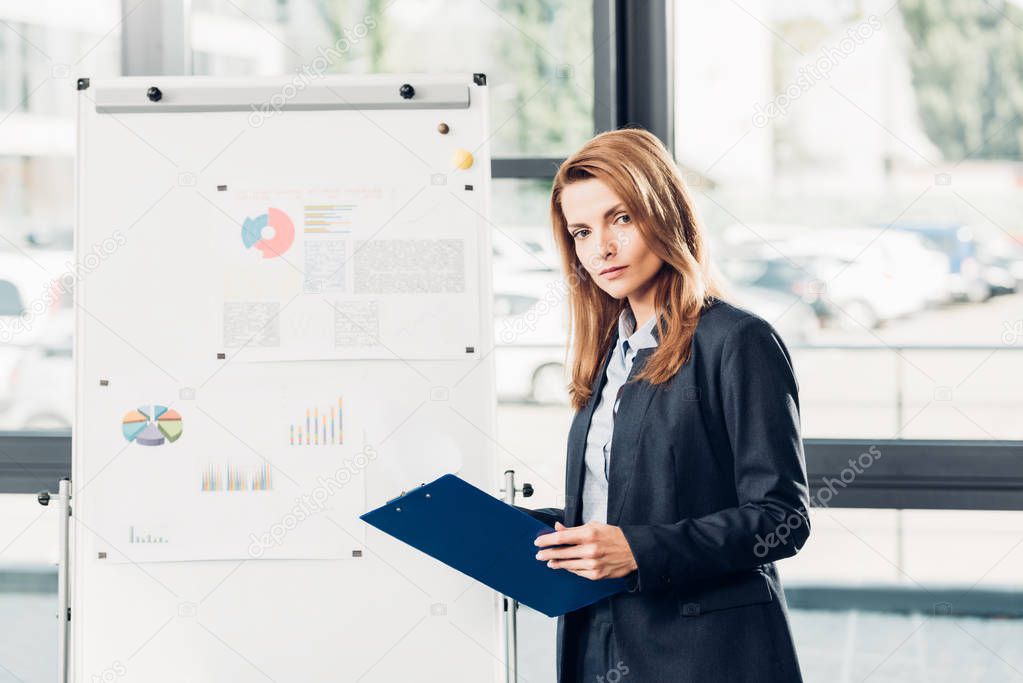 female business speaker with notepad standing at white board during lecture in conference hall