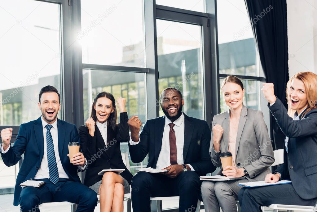 successful multiracial businesspeople sitting on chairs in conference hall
