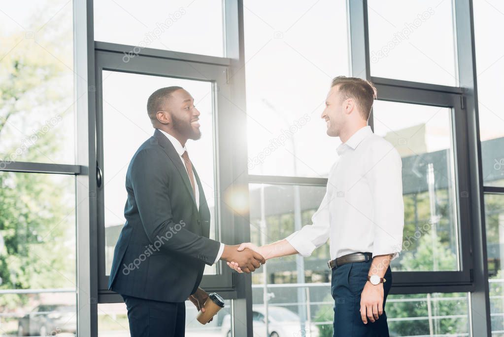 smiling multiracial business colleagues shaking hands in conference hall