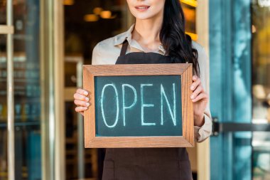 cropped image of cafe owner in apron holding open signboard near cafe clipart