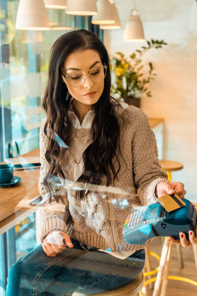 beautiful woman paying with credit card by contactless payment in cafe