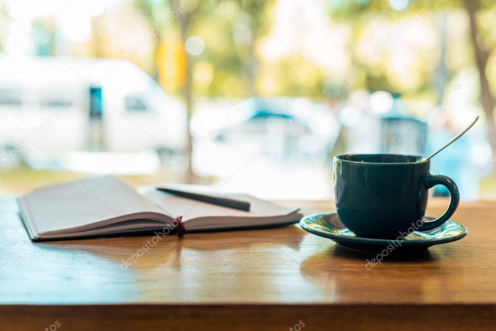 cup of coffee and open notebook with pen on wooden table in cafe