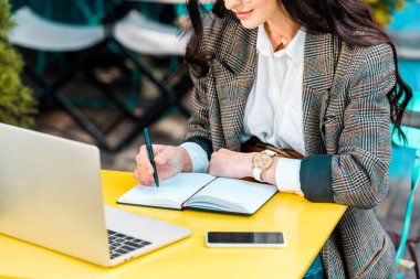 kadın freelancer planlayıcısı, smartphone ve dizüstü restoran terasında çalışma görünümünü kırpılmış