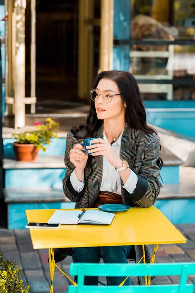美丽的自由职业者持有咖啡杯在咖啡厅露台与规划师和智能手机 — 图库照片