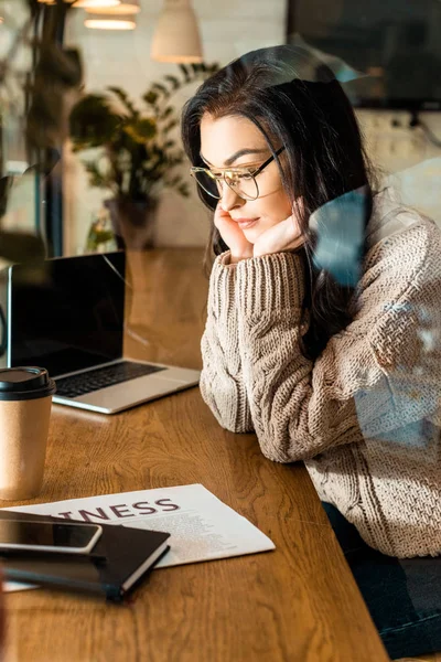 bored freelancer in cafe with laptop, smartphone and business newspaper