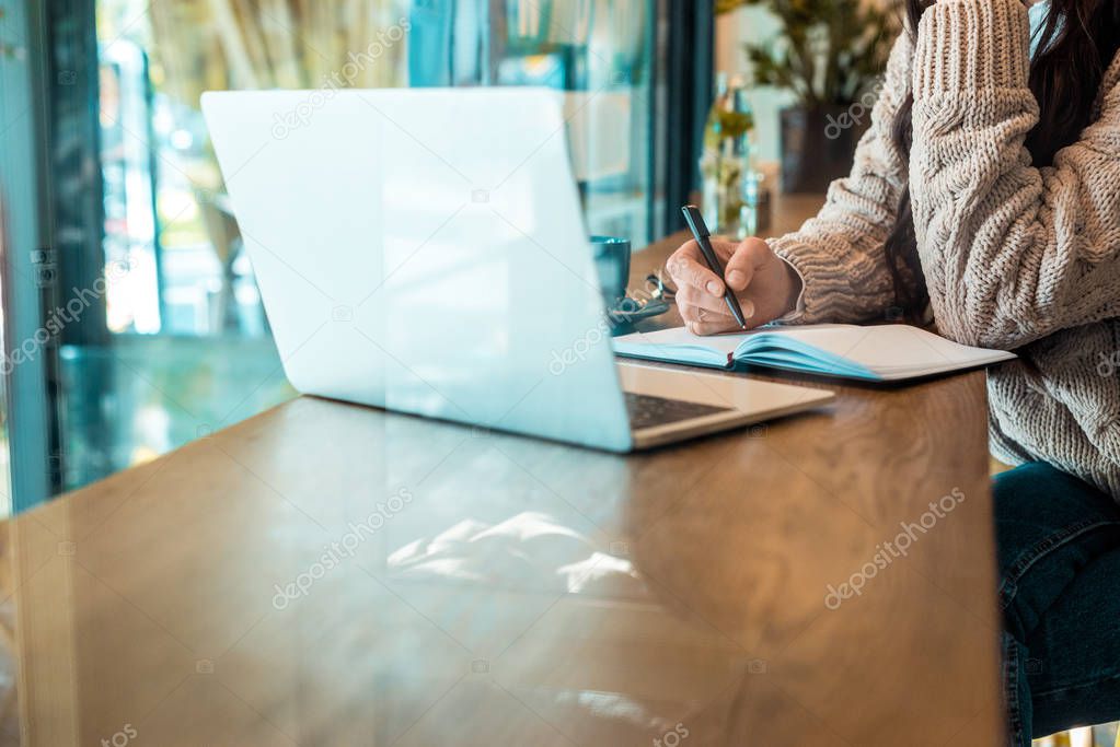 cropped view of freelancer working with planner and laptop in cafe 