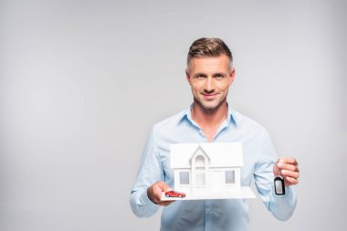 holding kağıt model araba alarmı uzak olan ev ve oyuncak araba beyaz izole yakışıklı yetişkin adam