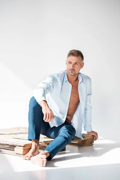 Schöner Sexy Mann Sitzt Auf Holzpalette Auf Weiß Und Schaut — Stockfoto