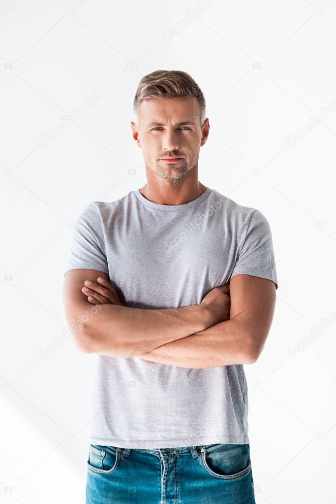 handsome adult man in blank grey t-shirt looking at camera with crossed arms isolated on white