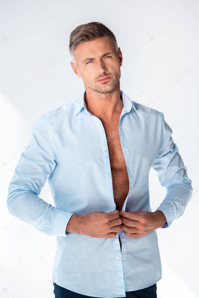 sexy macho buttoning shirt and looking at camera isolated on white