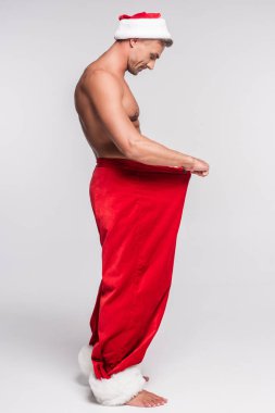 gömleksiz kaslı adam Noel Baba şapkası kırmızı pantolon içine gri görünümlü yan görünüm