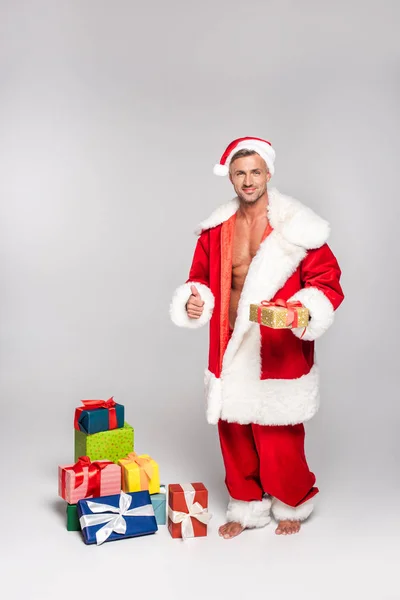 Sexy Man Santa Kostuum Holding Kerstcadeau Weergegeven Duim Omhoog Grijs — Gratis stockfoto