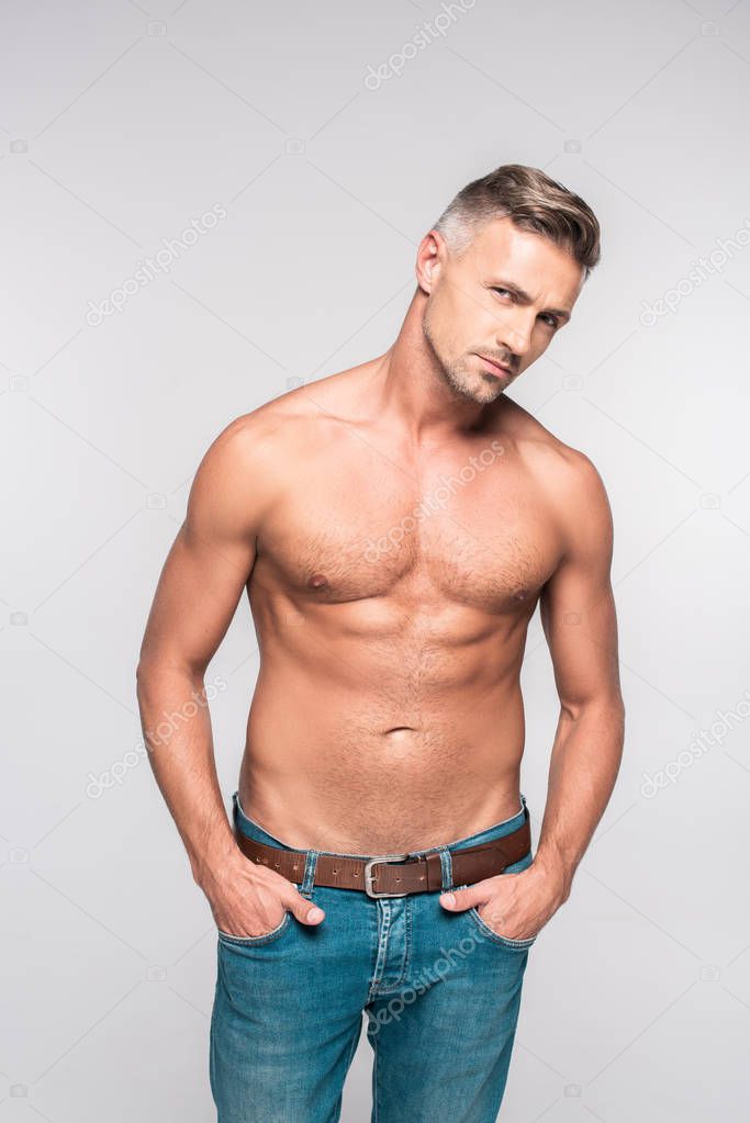 portrait of handsome shirtless man in denim pants looking at camera isolated on grey