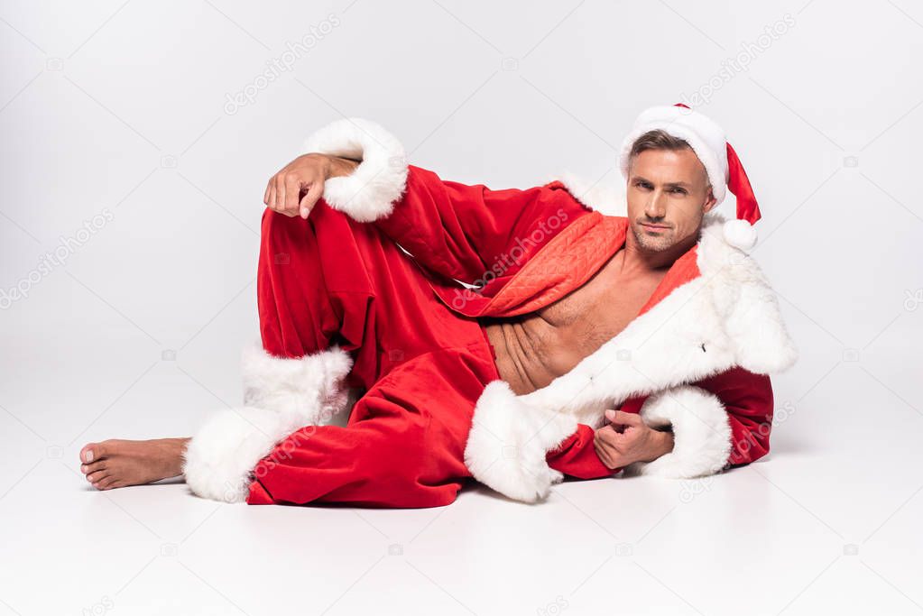 handsome sexy man in santa costume lying and looking at camera on grey