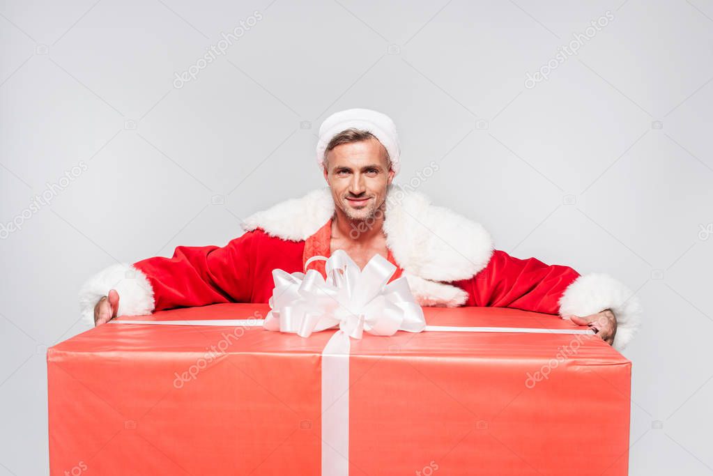 handsome santa claus holding big christmas present and smiling at camera isolated on grey