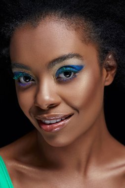 portrait of beautiful african american model with bright blue eyes shadows isolated on black clipart