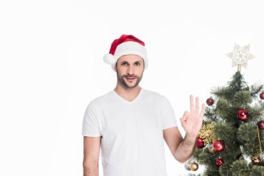 Noel ağacı üzerinde beyaz izole yakın dururken ok işaret gösteren santa claus şapka adam portresi