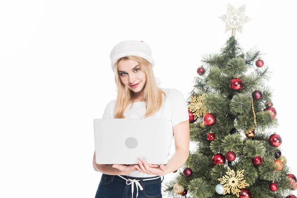 圣诞老人帽子的年轻妇女的肖像与笔记本电脑附近查出的圣诞树白色 — 免费的图库照片