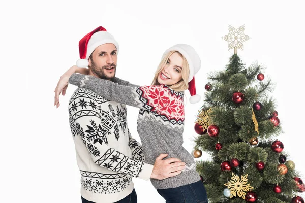 Young Couple Sweaters Santa Claus Hats Christmas Tree Isolated White — Stock Photo, Image