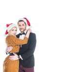 Portrait of fashionable couple in santa claus hats hugging isolated on white