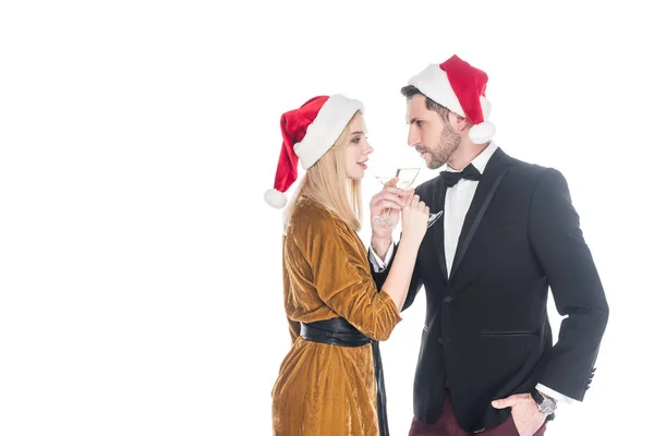 サンタ クロースの帽子は白で隔離シャンペンを飲んでのスタイリッシュなカップルの側面図  — 無料ストックフォト