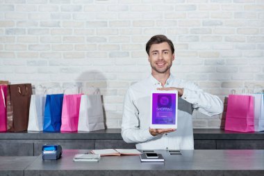 yakışıklı genç satıcı ile alışveriş uygulama ve kamera dükkanında gülümseyen dijital tablet holding  