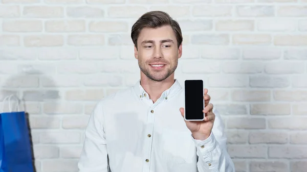 Uśmiechający Się Młody Człowiek Trzymając Smartfon Pustego Ekranu Podczas Pracy — Zdjęcie stockowe