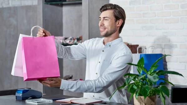 Sonriente Joven Vendedor Sosteniendo Bolsas Compras Mirando Hacia Otro Lado — Foto de stock gratuita