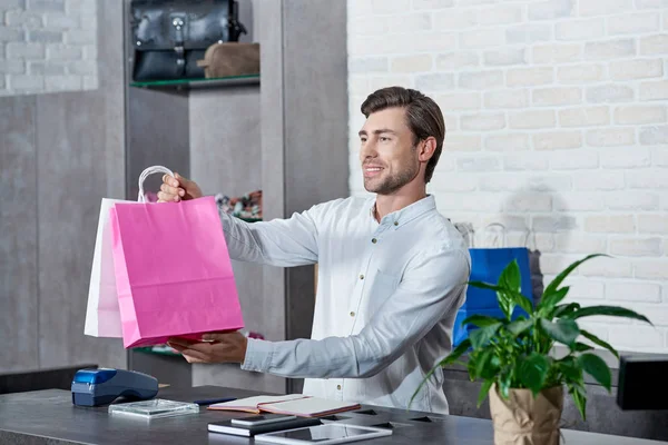 Smiling Young Salesman Holding Paper Bags Looking Away Store — Stock Photo, Image