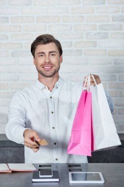gülümseyen genç satıcı dükkanda holding kağıt poşet ve kredi kartı