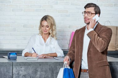 Alışveriş torbaları tutarak ve yanında smartphone kadın satıcı dükkanda not alma sırasında konuşurken gülümseyen adam 