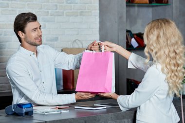satıcı ve genç kadın müşteri mağazada alışveriş torbaları tutmak gülümseyen 
