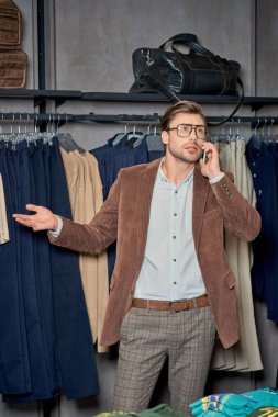 man in eyeglasses talking by smartphone while shopping in boutique    clipart