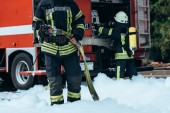 oříznuté záběr hasič ve vodní hadice v rukou stojící v pěna na ulici