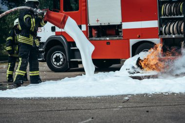 partial view of firefighter extinguishing fire with foam on street clipart
