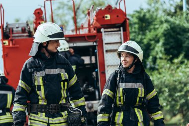 firefighters in protective uniform looking at each other on street clipart