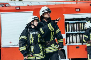 firefighters in protective uniform looking away with fire truck behind on street clipart