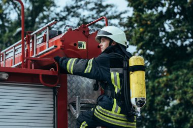 female firefighter with fire extinguisher on back standing on fire truck on street clipart