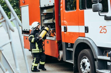 female firefighter in protective uniform putting fire extinguisher into truck on street clipart