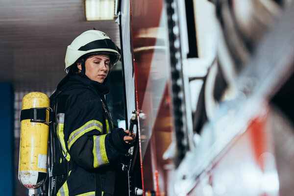 side view of female firefighter with fire extinguisher on back closing truck at fire station