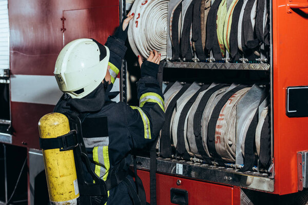 partial view of female firefighter putting water hose into truck at fire department
