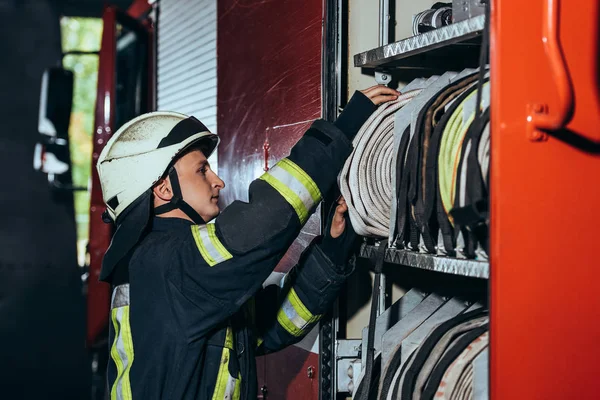 Zijaanzicht Van Brandweerman Beschermende Uniforme Controle Apparatuur Vrachtwagen Bij Brandweerkazerne — Stockfoto