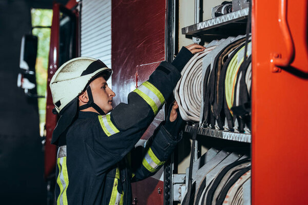 side view of fireman in protective uniform checking equipment in truck at fire station