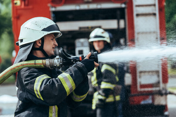 selective focus of firefighter with water hose extinguishing fire on street