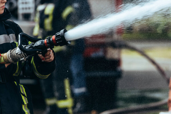 partial view of firefighter with water hose extinguishing fire on street