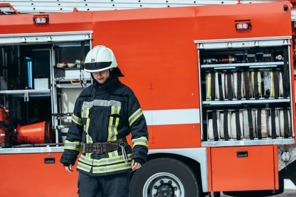 Чоловічий Пожежник Формі Стоїть Вулиці Червоною Пожежною Машиною Позаду — Безкоштовне стокове фото
